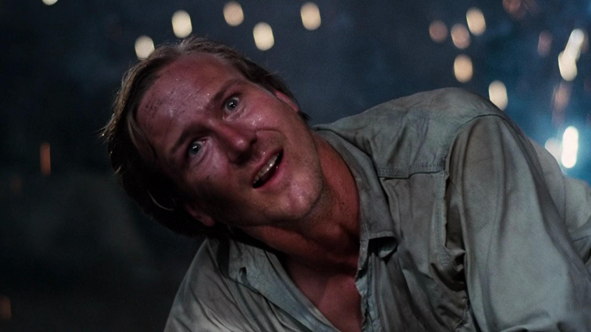 Nighttime, with blurred lights in the background. A man covered in sweat and filth, whose face expresses a mixture of ecstasy and horror.