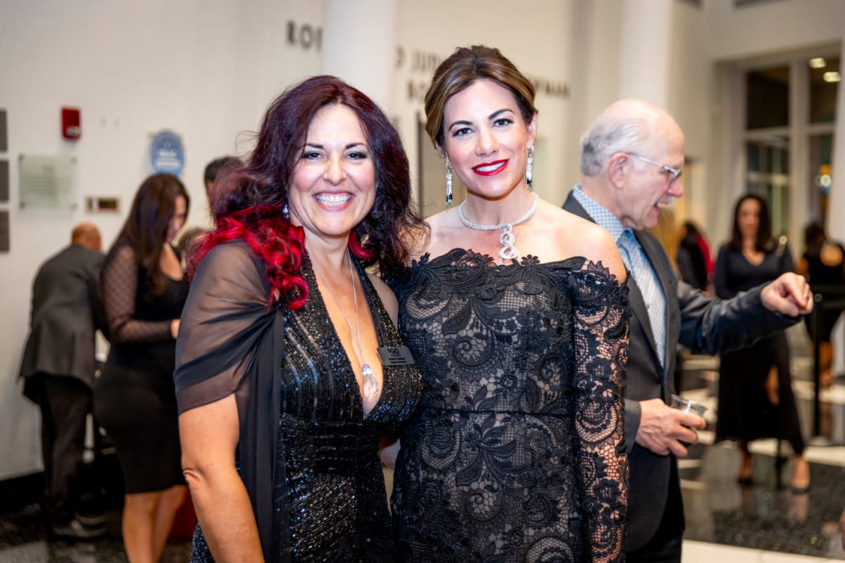 This is a photo of FGO General Director Maria Todaro and FGO Board Chair Tina Vidal-Duart. They are at a fancy opera event and wearing stunning gowns and jewelry. They are both smiling broadly.