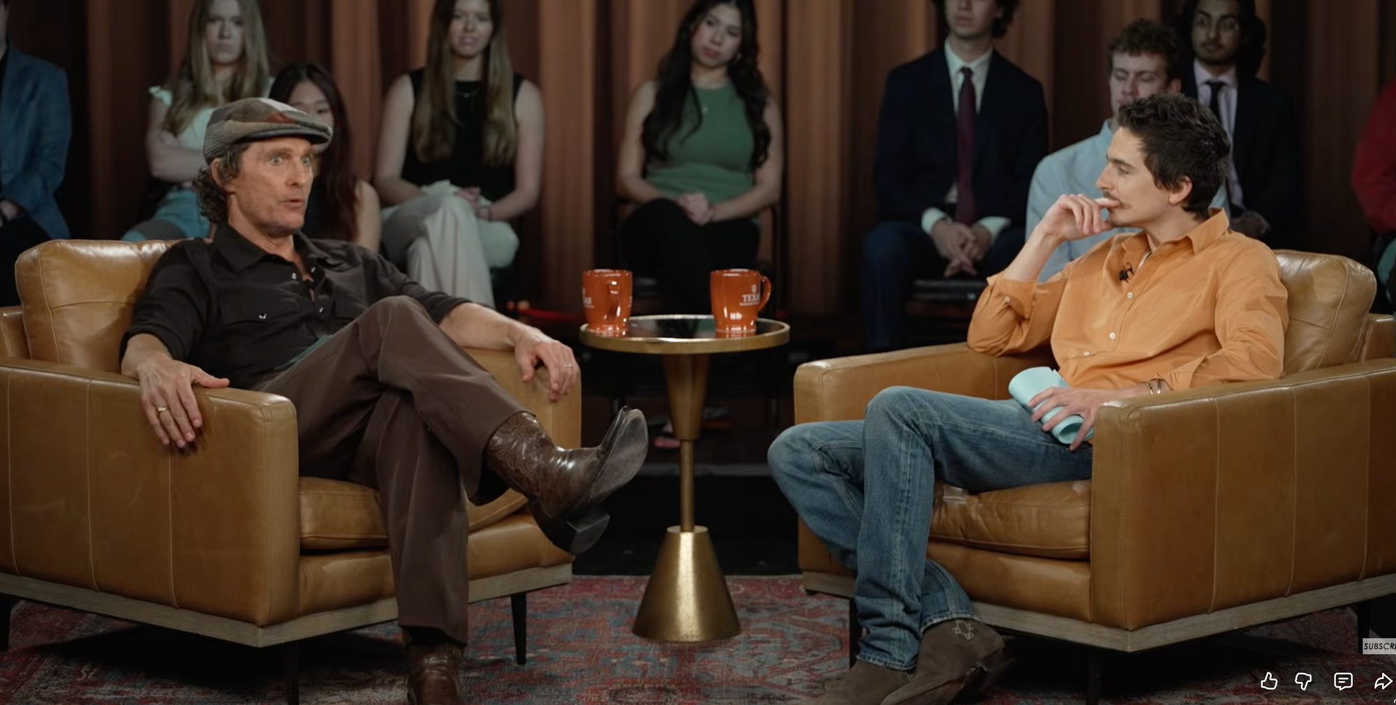 Two white guys have a conversation while seated in comfy chairs. The white guy on the left is older and a little wiser than the white guy on the right.